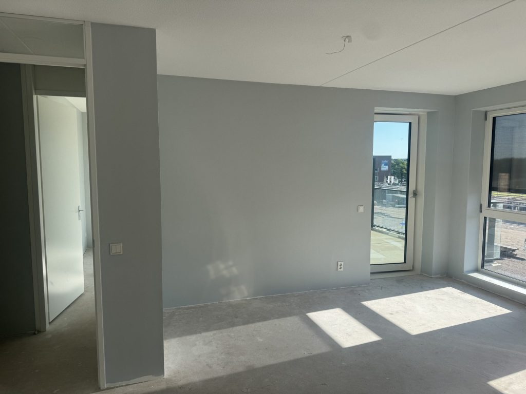 Kamer in een appartement met lichtgrijs gesausde wanden en zon op de betonvloer