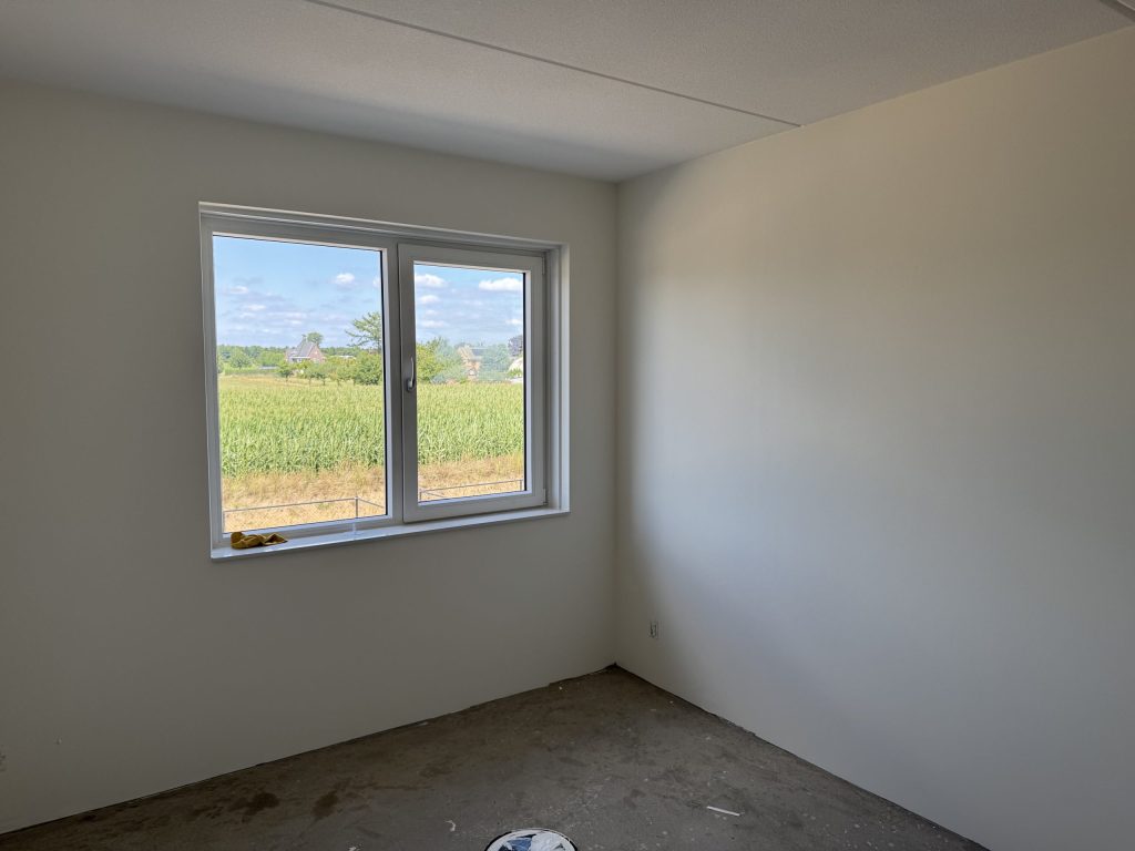 Kale slaapkamer in een nieuwbouwhuis met strakke witte wanden en uitzicht op een weiland