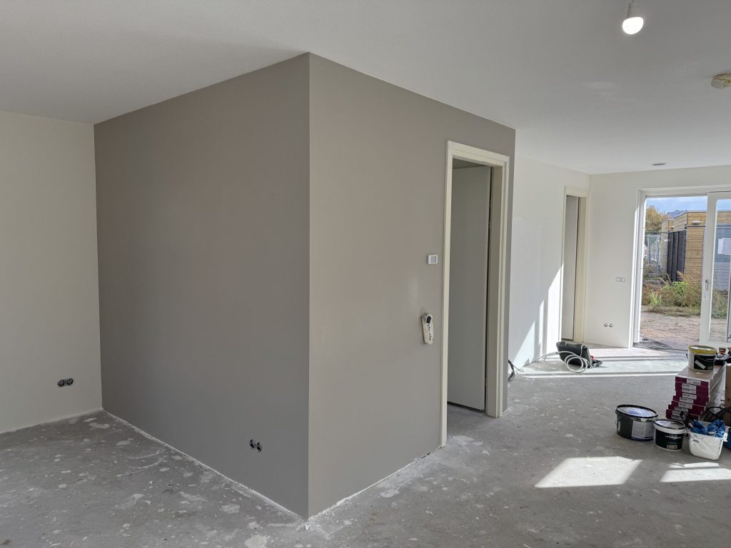 Woonkamer van een eengezinswoning met taupe gesausde muren rond de trapkast
