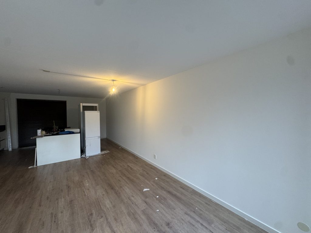 Lange woonkamer met open keuken en strakke witte wanden na het behangen