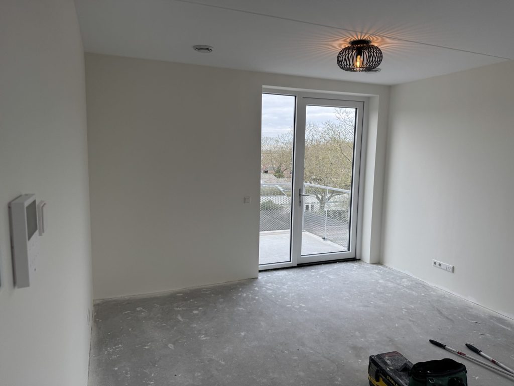 Lege kamer in een nieuw appartement met witte renovliesmuren en deuren naar het balkon