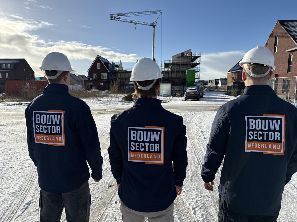 Drie vakmensen van Bouwsector Nederland met witte helm op een besneeuwde bouwplaats tussen nieuwe huizen